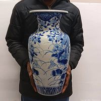 Front view of the vase held by a person to show scale, featuring blue floral and bird designs on white porcelain.