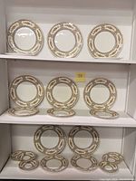 Two shelves with Aynsley Keswick patterned dinnerware including plates and saucers in floral and leaf design with gold and brown accents.