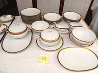Photo showing full set of Bavarian fine china dishes and serving pieces with white porcelain and gold rims arranged on table.