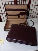 Brown briefcase laid open with visible interior compartments and combination lock on the side.