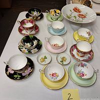 Table overview showing pastel and black floral teacup and saucer sets alongside cake dish