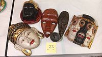 Five wooden hand painted masks arranged on table with small pottery cup.