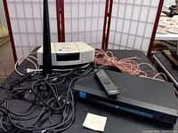 Bose Wave CD stereo in white, Sony DVD/CD player in black with remote on top, Terk indoor antenna, and cables on a black surface with a folding screen background.