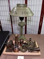 Full view of green enamelware lamp with floral decoration and wooden tray holding various brass and silverplated items including candlesticks, vase, elephant figurine, and small pitchers.