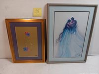 Two framed lithographs side by side: the floral lithograph with a gold frame on the left and the Bill Rabbit lithograph in a gray frame on the right.