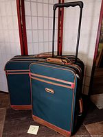 Front and side view of the green Jaguar brand rolling carry-on suitcase with extended handle, alongside matching large suitcase in the background.