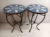 Side view of both round mosaic tables showing blue and white geometric patterned ceramic tops and black metal legs.