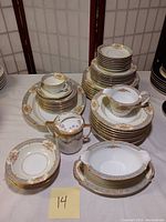 Full view of stacked Noritake and Nippon fine china set showing plates, cups, sugar bowl, creamer, and serving pieces, all with floral pattern and gold trim.