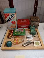 Full view of all items on wooden tray showing different tins, toys, coin bank, harmonica, and collectibles