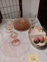 Overview of pink glass stemware, small glass bowls, plates and Franciscan divided dish with salt and pepper shakers on table.