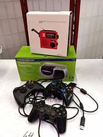 Overview photo showing the Grundig emergency crank radio box, Sylvania radio cassette recorder box, two Xbox 360 controllers, Sony PlayStation controller with cords tangled together.