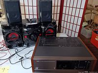 LG CM4360 mini hi-fi stereo system main unit with red-accented large speakers and satellite speakers alongside Kyocera R-851 tuner/amplifier on table