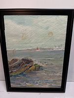 Front view of textured oil seascape painting on wood panel with rocks, lighthouse, ship, and sky in black frame.