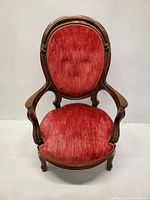 Front view of Victorian style armchair showing red velvet tufted backrest, plush seat cushion, and ornate wooden frame with curved armrests and legs.