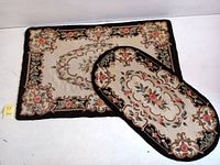 Pair of rugs, one rectangular and one oval, displaying floral hooked and tufted patterns with cream background and black borders.