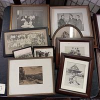 Wide view of a collection of framed vintage photographs on a table showing group portraits, family photos, children with pets, and formal images of men.