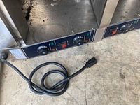Close-up of commercial food warmer control panel showing two temperature knobs, power button, and indicator lights. Black power cord visible.