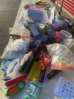 Wide view showing assorted educational supplies including magnifying glasses, nets, buckets, sand timers, brushes, and other learning tools grouped on a table and partially packed in clear plastic bags.