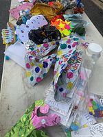 Foil balloons and party supplies spread on white table, various colors including polka dots balloon, partially deflated balloons and colored paper cutouts visible.