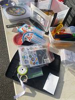 Overview of plastic bins showing educational flashcards, felt patches with rainbow design, crayons, markers, colored pencils, and crafting tools on a table.