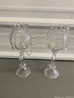 Full view of two clear glass candle holders with hexagonal bases and beaded chains hanging from scalloped rims.