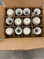 Top view of the box containing 12 mini white ceramic vases separated by cardboard dividers.