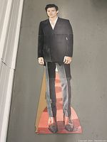 Full-body front view of the Harry Styles cardboard standee lying on the floor, showing black suit, white shirt, and brown shoes printed on it