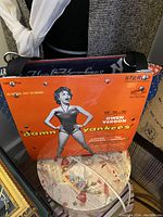 Purse shown with front panel made from Gwen Verdon 'Damn Yankees' album cover, orange color, featuring a black and white photo of Gwen Verdon. Navy blue interior lining with white New York Yankees logo and script visible inside purse.
