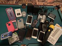 Photo showing a mix of cellphones, phone cases, portable speakers, a video camera, and assorted electronic accessories arranged on a surface.