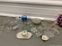 Photo of assorted glassware items on table, including serving trays, bowls, glasses, vases, and some ceramic pieces