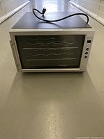 Front view of the Intertek thermoelectric wine cooler with glass door, metal handle, and power cord coiled on top.