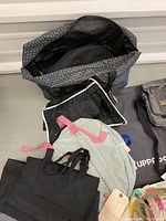 Overview of six bags including a large patterned tote bag, a mint green backpack with pink straps, a black tote bag, gray backpack, and black messenger bag.