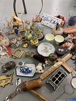 Photo showing a collection of various small decorative and collectible items including figurines, plates, cups, and a wooden crucifix.