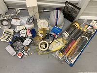 Photo of a mixed lot including a helmet, calculator, electrical components, and tools spread on the floor.