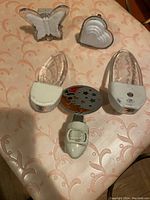 Five assorted night lights on peach patterned fabric surface including butterfly, heart, two leaf-shaped clear lights, and crescent moon light with stars.