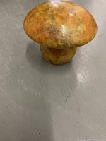 Front view of a small polished stone mushroom figurine with an orange and brown marbled pattern on a gray surface.