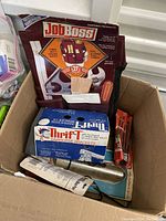 Cardboard box containing Job Boss tool bag, Thrift sawhorse bracket box, a wooden block, and other loose tools seen from above.