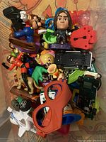 Top-down view of a pile of assorted plastic toys and figurines in a container showing characters, vehicles and toy glasses.