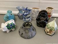 Seven assorted decorative items on a white surface including vases, piggy banks, and figurines.