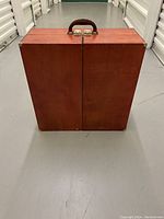 Closed wooden case with leather-style handle and metal latches on top, showing the exterior of the carrying bedroom wardrobe.