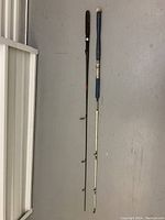 Two fishing poles lying on a grey floor side by side, showing overall length and condition.