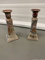 Pair of ceramic candle holders with colorful floral patterns placed on floor, showing overall design and shape.