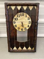 Front view of the vintage stained glass clock showing the wooden frame, stained glass panels, and round clock face with black numbers.