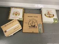 Photo showing three vintage wooden cigar boxes with decorative logos and text - Macanudo, Las Cabrillas Columbus Natural, and El Rey del Mundo Tabacos de Honduras.
