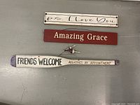 Three wooden hanging signs with inscriptions and a small bird figurine displayed on a grey surface.