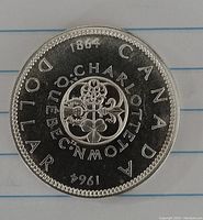 Close-up image of the reverse side of the 1964 Canadian silver dollar. Shows the years 1864 and 1964 with the floral emblem and text around it.
