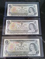 Front view of three 1973 Canadian one dollar bank notes in plastic sleeves