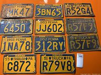 Top-down view of all 11 Pennsylvania license plates from the 1949-1957 period arranged flat on an orange surface showing various conditions and designs