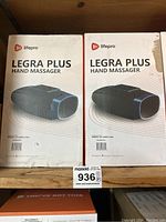 Photo showing two boxed Lifepro Legra Plus hand massagers side by side on a shelf, boxes appear new with slight edge wear.