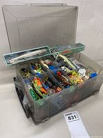 Closed view of clear 2-sided Plano tackle box showing compartments filled with various lures and accessories